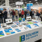 A display of marketing materials in vibrant blue, green and white color combinations at a table in a networking event full of people