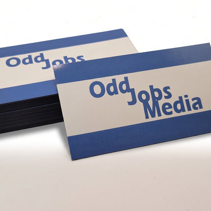[photo] A stack of rectangular business card magnets with a white center, blue top and bottom bands, and the text 'Odd Jobs Media' printed in blue, photographed on a plain white background.