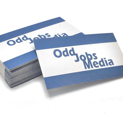 [photo] A stack of rectangular business cards with blue and white horizontal stripes and the text 'Odd Jobs Media' printed in blue, photographed on a pure white background.