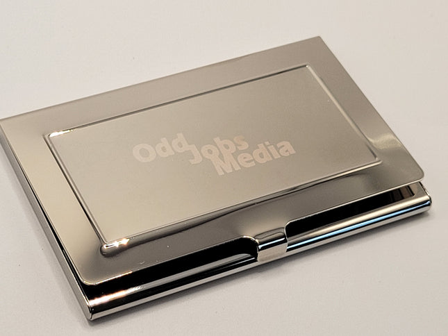 A polished silver metal business card holder with a hinged cover, featuring the text 'Odd Jobs Media' debossed on the front, set against a plain light background.