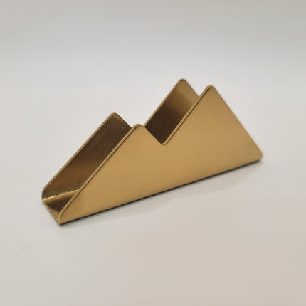 A small metallic gold triangular holder or stand with a matte finish, photographed on a plain light gray background.
