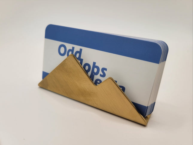 A gold-colored metal mountain-shaped card holder displaying a blue and white card with the text 'Odd jobs'.