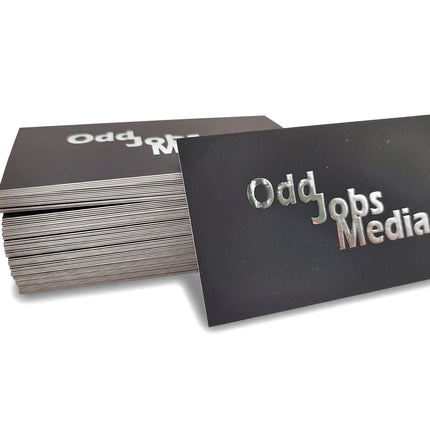 [photo] A stack of black business cards with metallic silver foil text reading 'Odd Jobs Media' on a pure white background.