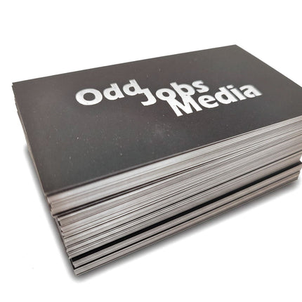 [photo] A stack of black business cards printed with the white text 'Odd Jobs Media', photographed on a pure white background.