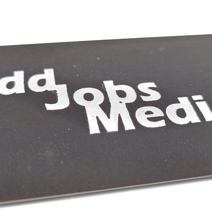[photo] A close-up of a black business card with the words 'Odd Jobs Media' in large white stylized lettering, photographed on a pure white background.