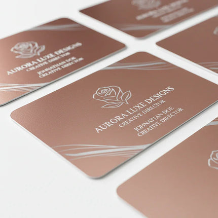 Rose gold plastic business cards with silver printing and rounded corners on white background